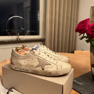 Golden Goose Deluxe Brand Super Star Low-Top Sneakers - Säljer nu tyvärr mina otroligt snygga vita sneakers från Golden Goose som passar till alla stilar | Skick 8,5/10 skorna har blivit regelbundet impregnerade | Köpt på Cettire med nypris ca 5000kr | Mitt pris 2999kr | Pris går att diskutera!! | Tveka inte att ställa frågor.