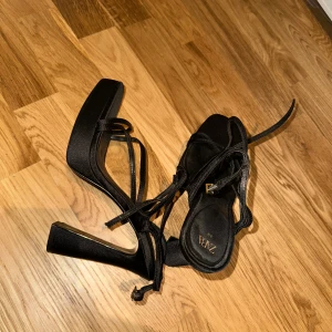 Svarta platå klackskor från Zara - Svarta klackskor från Zara med knytband och fyrkantig tå. Klackarna ger en elegant touch och knytbanden ger en unik stil. Endast använt en gång och köpt sommaren 2024.