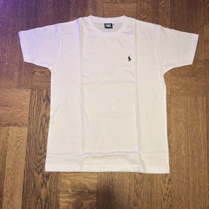 Vit t-shirt från Polo Ralph Lauren - Säljer en klassisk vit t-shirt från Polo Ralph Lauren med det ikoniska broderade logotypen på bröstet. T-shirten är kortärmad och tillverkad i mjuk bomull för en bekväm passform. Perfekt för en stilren look.