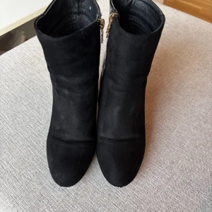 Svarta stövletter med krokodilmönster - Snygga svarta stövletter med en unik krokodilmönstrad detalj på hälen. De har en klack och spetsig tå, vilket ger en elegant look. Perfekta för att lyfta vilken outfit som helst.