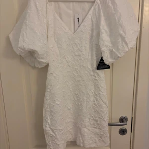 Vit brokadklänning från Gina Tricot - Säljer en elegant vit brokadklänning från Gina Tricot med puffiga ärmar och v-ringning (Brocade dress). Klänningen har en dragkedja i ryggen och är perfekt för speciella tillfällen som studenten! Den är i storlek 34 och har en vacker textur som ger en lyxig känsla. Klänningen är endast testad, lägger ut här då den är helt slutsåld🤍