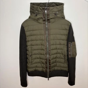 Moncler cardigan storlek M - Snygg grön quiltad jacka från Moncler med stickade ärmar och huva. Jackan har en dragkedja framtill och en praktisk ficka med dragkedja på ärmen. Perfekt för kyliga dagar med sin stilrena design och bekväma passform. Priset går att diskutera vid snabb affär finns kvitto kan tilldelas vid förfrågan, finns inga defekter eller liknande den är i topp skick. Nk box tillkommer vid köp.