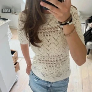 Beige stickad/virkad trekvartsärmad topp - Snygg beige stickad topp med korta ärmar och ett vackert hålmönster. Perfekt för en stilren och avslappnad look. Passar bra till både jeans och kjol.
