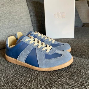 Maison Margiela - Snygga blå sneakers från Maison Margiela med beige snörning och gummisula. Skorna har en mix av mocka och skinn. Dem är i storlek 43 och är i nytt skick. Orderbekräftelse finns och allt OG följer med. Skriv om ni har funderingar eller frågor! :)