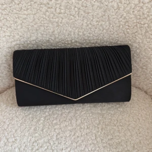 Svart kuvertväska med gulddetalj, bal väska  - Stilren svart kuvertväska med veckad framsida och guldfärgad kant. Väskan har en kedjerem i guld och stängs med magnetlås. Perfekt nu till pallen, postar snabbt. Råkade beställa två lika dana så du får såklart den som är oöppnad!❤️❤️