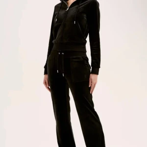 Svarta mjukisbyxor i velour - Svarta mjukisbyxor i mjuk velour med dragsko i midjan och fickor med knappdetaljer bak. Byxorna har en relaxed passform och lätt utsvängda ben. Perfekta för en chill och avslappnad stil.