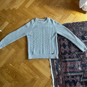 Ljusgrå stickad tröja från Pier One - Säljer en ljusgrå stickad tröja från Pier One med klassiskt flätmönster framtill. Tröjan har rund halsringning och långa ärmar. Perfekt för kyligare dagar och enkel att matcha med olika outfits.