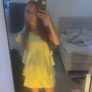 Gul volangklänning från Zara - Säljer en ljusgul klänning från Zara med flera volanglager och oneshoulder-design. Klänningen har en luftig passform och är perfekt för varma dagar. Tillverkad i ett lätt och syntetiskt material.