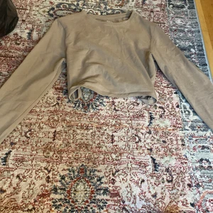 Beige croppad långärmad tröja - Säljer en beige croppad långärmad tröja med rund halsringning. Perfekt för dig som gillar en enkel och stilren look. Mjuk och skön bomullskänsla, passar till många outfits.