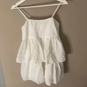 Vit volangklänning med smala axelband från Gina Tricot, perfekt till skolavslutning  -  Söt vit klänning från Gina Tricot med smala axelband och volanger. Klänningen har små glittriga detaljer i tyget och smock baktill för extra komfort. Perfekt för varma dagar och somriga tillfällen.