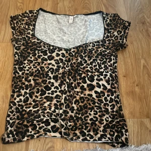 Leopardmönstrad topp från Nelly - Säljer en leopardmönstrad topp från Nelly med v-ringning och svarta spetsdetaljer längs halsringningen. Toppen har korta ärmar och är tillverkad i ett mjukt, stretchigt material. Den är använd 2-3 ggr. Jag säljer den pågrund av att den inte kommer till användning. Den är perfekt för dig som vill ha något med leopardmönster eller en fin detalj på din outfit. Pris kan diskuteras.💕