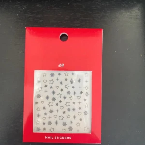 Nagelstickers med stjärnor och hjärtan från H&M - Nagelstickers från H&M med motiv av små stjärnor, hjärtan och snöflingor i svart och silver. Perfekt för att dekorera naglarna med olika mönster. Kommer i en röd förpackning.