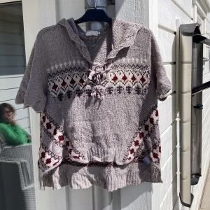 Stickad hoodie med mönster från Cream - Mysig stickad hoodie i ljusbeige från Cream, storlek S/M. Tröjan har korta ärmar, huva och ett klassiskt mönster i rött, vitt och grått. Materialet är en blandning av akryl och mohair. Perfekt för lager-på-lager och chill dagar.