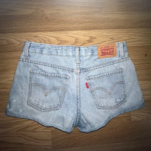 Levi's Girlfriend Shorty jeansshorts - Säljer ett par ljusblå jeansshorts från Levi's modell Girlfriend Shorty. Klassisk femficksdesign, låg midja och råa benslut. Slitna detaljer framtill för en avslappnad look. Perfekta för varma dagar.