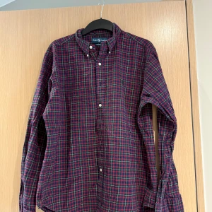 Rutig skjorta från Ralph Lauren - Säljer en klassisk rutig skjorta från Ralph Lauren i mörkblått och rött. Måttet är cirka 67cm lång och 47cm bred. Storleken är L och skicket är bra om ni stryker den kommer den se som ny ut🤩 Nypris cirka 1600kr