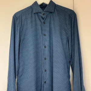Skjorta - Säljer nu en riktigt fet Skjorta ifrån Baldessarini. Skjortan är i storlek M men kan även passa de som har S som storlek. Skjortan är blå färgad men har små mönster som bildar en elegant look💪Skjortan är rätt använda men har inga defekter som syns. Vid frågor hör gärna av er🤝