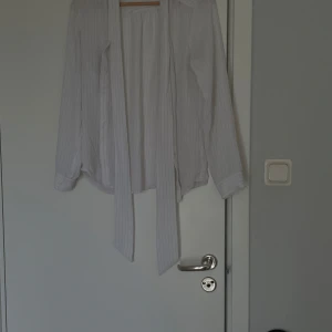 Köp 1 få 2  - Säljer en vit blus från Stockh LM i storlek 40. Blusen har tunna grå ränder, långa ärmar och långa knytband framtill. Materialet känns lätt och luftigt, perfekt för en stilren look.