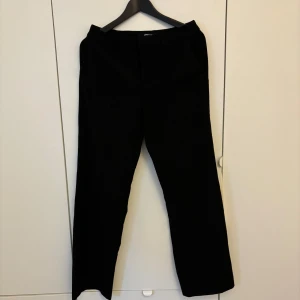 Svarta kostymbyxor från Gina Tricot - Klassiska svarta kostymbyxor från Gina Tricot i storlek 36. Byxorna har rak passform och normal midja. Tillverkade i ett mjukt och bekvämt material som passar året runt.