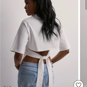 Vit t-shirt med rosett i ryggen från Nelly - Säljer en vit T-shirt  från Nelly med knytband som man kan knyta till en rosett på ryggen. Man kan använda tröjan i sin vardag men också om man vill vara finklädd. Den är använd ca 5 ggr. Den har ett jättebra skick. Jag säljer den för att jag inte använder den så mycket. Pris kan diskuteras 