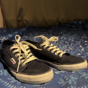 Svarta sneakers från Helly Hansen - Säljer ett par mörkblåa sneakers från Helly Hansen med vita snören och vit sula. Skorna har en liten logotyp på sidan och ankare på hälen. Perfekta för en avslappnad stil och passar till det mesta. Köptes för 950kr flera år sedan men säljs för 500kr eftersom jag bara använt de 2 gånger
