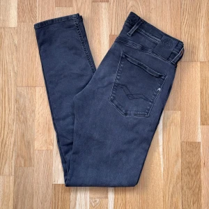 Replay Anbass Svarta Jeans - Replay jeans i modellen Anbass och färgen svart, finns ett litet hål, syns på fjärde bilden. Sedan ett till hål en bit under gylfen, syns på sista bilden. Storlek: 31 W 32 L, Midja: 40 cm Ytterben: 103 cm Benöppning: 15.5 cm Material: 88% Cotton, 8% Polyester, 4% Elastane.