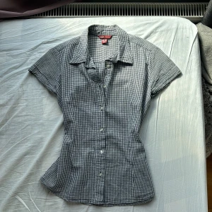 Svartvit rutig skjorta från H&M L.O.G.G. - Säljer en svartvit rutig skjorta från H&M L.O.G.G. med korta ärmar och klassisk krage. Skjortan har figurnära passform och knäppning framtill. Perfekt för en stilren och avslappnad look.