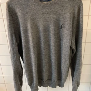 Grå merinoulltröja från Polo Ralph Lauren - Säljer en stilren grå långärmad tröja från Polo Ralph Lauren i merinoull. Tröjan har en slim passform och klassisk rund halsringning. Diskret broderad logga på bröstet.