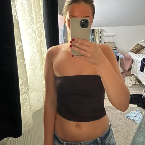 Brun tubtopp - Säljer en enkel brun tubtopp som sitter tight runt överkroppen. Perfekt att matcha med jeans eller kjol för en stilren look. Toppen är ärmlös och har en klassisk, minimalistisk design.