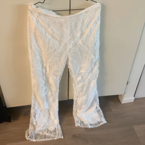 Vita spetsbyxor med utsvängda ben - Säljer ett par vita byxor i spets med blommigt mönster och utsvängda ben. Byxorna har vita inbyggda underbyxa.