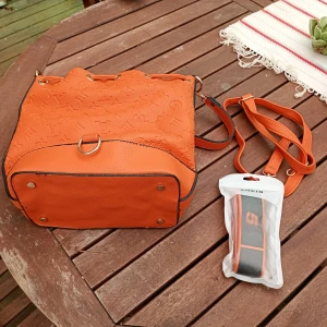 Orange bucket bag med präglat mönster - Säljer en orange bucket bag med präglat mönster och justerbar axelrem. Väskan har dragskostängning och detaljer i guld. Insidan är fodrad med röd- och svartmönstrat tyg och har en innerficka med dragkedja. Perfekt för dig som vill sticka ut med färg. Från Shein.