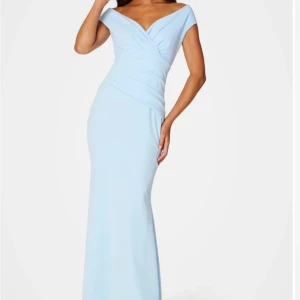 Ljusblå långklänning med v-ringning - Elegant ljusblå balklänning med v-ringad omlott-topp och offshoulder-skärning. Klänningen har figurnära passform och är perfekt för festliga tillfällen. Tillverkad i ett mjukt, slätt material som ger en lyxig känsla. Slutsåld på hemsidan!!❤️