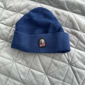 Blå mössa från Parajumpers - Snygg blå mössa från Parajumpers med uppvikt kant och broderad logotyp framtill. Tillverkad i ribbstickat material som ger en klassisk och stilren look.