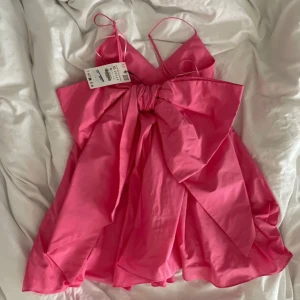 Rosa miniklänning med stor rosett - Supersöt rosa miniklänning med smala axelband och en stor rosett bakom, helt ny!