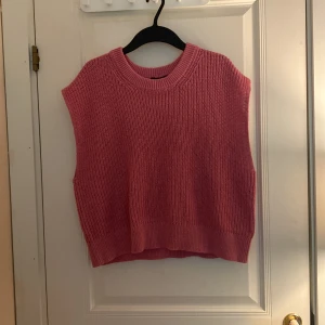 Rosa stickad väst från Lindex - Säljer en rosa stickad väst från Lindex i storlek M. Västen har en rund halsringning och breda ribbade kanter vid hals och nederkant. Perfekt att styla över en skjorta eller t-shirt för en trendig lager-på-lager-look.