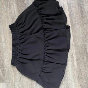 Svart volangkjol från new yorker  - Säljer en svart kortkjol med bred resår i midjan och volangdetaljer. Kjolen är luftig och har en snygg, avslappnad passform. Perfekt att styla med en enkel topp eller hoodie.