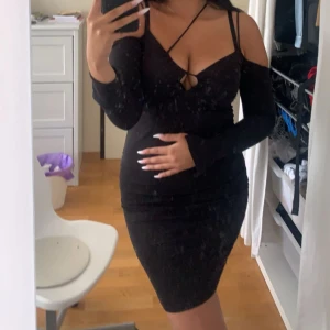 Svart tight klänning med lång ärm och snörning - Säljer en svart tight klänning med lång ärm och snygg snörningsdetalj framtill. Klänningen har en djup v-ringning och axelbandsdesign som ger en trendig look. Perfekt för dig som vill sticka ut! Passar S och M