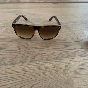 Bruna boyfriend-solglasögon från Ray-Ban - Snygga botfriend-solglasögon från Ray-Ban i brunmelerad färg med klassisk fyrkantig form. Glasen är tonade och bågarna har Ray-Ban-logga på sidan. Perfekt accessoar för soliga dagar. Tillkommer inget kvitto eller box