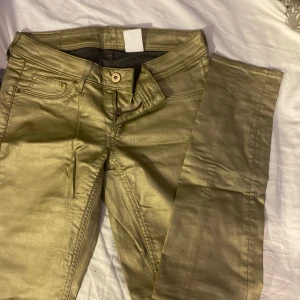 Guldiga super skinny jeans H&M - Snygga guldiga super skinny jeans från H&M med låg midja. Byxorna har klassisk femficksdesign, dragkedja och knapp framtill. Materialet är denim med en metallic finish som verkligen sticker ut.