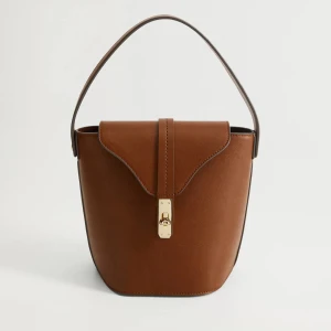 Box bag med gulddetalj - Stilren brun bucket handväska i skinnimitation med snygg guldfärgad låsdetalj framtill. Väskan har ett stadigt handtag och minimalistisk design som ger en clean look. 