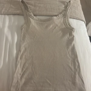 Beige ribbad linnetopp - Säljer en stilren beige linnetopp med smala axelband och ribbad struktur. Perfekt för varma dagar eller som lager under en skjorta. Enkel och clean design som passar till det mesta.