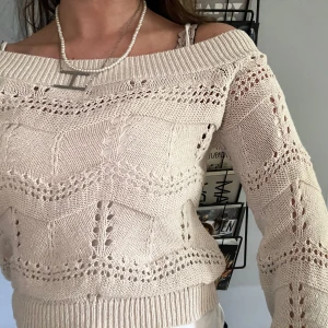 Beige offshoulder stickad tröja ONLY - Superfin beige stickad tröja från ONLY med offshoulder-modell och snyggt hålmönster. Tröjan har långärmade, lite pösiga ärmar och bred ribbad kant upptill och nedtill. Perfekt för dig som vill ha en chill men ändå söt look.
