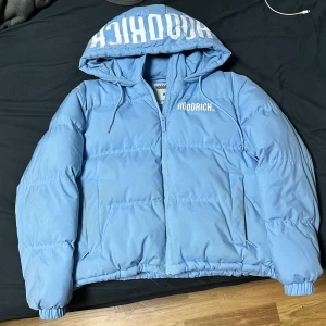 Ljusblå pufferjacka Hoodrich - Säljer en ljusblå pufferjacka från Hoodrich i storlek XS men det passar för S eller M. Jackan har huva med stor vit logga, dragkedja framtill och två fickor. Perfekt för kalla dagar i sverige.