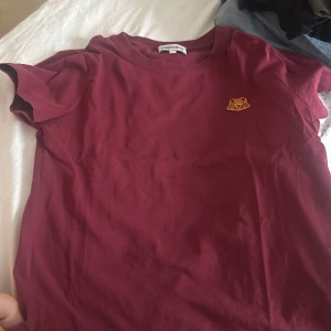 Vinröd t-shirt från Kenzo med tigerpatch - Vinröd t-shirt från Kenzo i bomull med klassisk passform och korta ärmar. På bröstet sitter en broderad tigerpatch i gult och orange. Perfekt basic med en snygg detalj som lyfter hela outfiten.