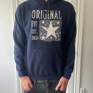 Mörkblå hoodie ifrån Scndi med stjärntryck - Säljer en mörkblå hoodie från Scndi med stor vit stjärna och texten 'Original Fit Est. 2024' på bröstet. Tröjan har huva, magficka och är tillverkad i en mjuk blandning av bomull och polyester. Perfekt för dig som gillar streetstyle och bekväma plagg.