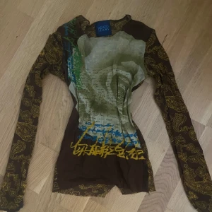 Mönstrad långärmad topp från Kenzo Jeans - Säljer en unik långärmad topp från Kenzo Jeans i brunt med gult paisleymönster och coolt tryck framtill i grönt, blått och gult. Tunn och stretchig med figurnära passform, perfekt för dig som gillar statement-plagg och konstnärliga prints.