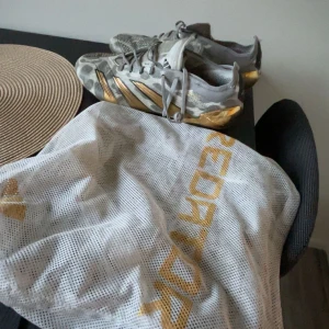 Adidas Predator Elite - Säljer ett par Adidas Predator fotbollsskor i grått och guld med coolt kamouflagemönster. Skorna har snörning och guldiga detaljer på sidorna och sulan. Perfekta för dig som vill sticka ut på planen! Medföljer originalpåse. De säljs inte längre och är väldigt svåra att få tag på. Pris är diskuterbart!