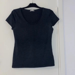 Mörkgrå basic topp med kort ärm - Enkel och stilren mörkgrå topp med rund halsringning och korta ärmar. Perfekt att matcha med jeans eller kjol för en clean look. Figurnära passform och mjukt material som känns skönt mot huden.