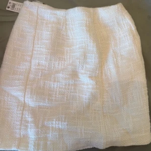 Vit tweedkjol från Gina Tricot - Supersnygg vit kort tweedkjol från Gina Tricot i storlek 34. Kjolen har en klassisk rak passform och är tillverkad i ett strukturerat tyg med dragkedja i sidan. Perfekt att styla med en enkel topp eller kavaj för en chic look.