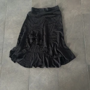 Svart långkjol från Amisu, strl 36 - Svart långkjol från Amisu i storlek 36. Kjolen har en lätt glansig yta, volang nertill och resår i midjan för skön passform!❤️