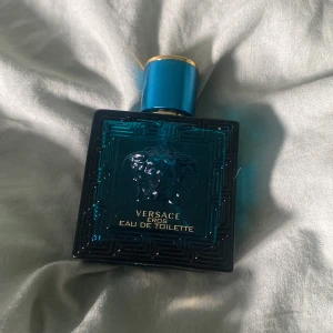 Versace Eros Eau de Toilette 50ml - (40 procent kvar av perfymen) box kommer med )Versace Eros Eau de Toilette i en snygg turkosblå glasflaska med guldiga detaljer och Medusa-huvudet på framsidan. Flaskan rymmer 50 ml och har en lyxig, maskulin design med geometriskt mönster. Perfekt för dig som gillar exklusiva dofter och stilren look.